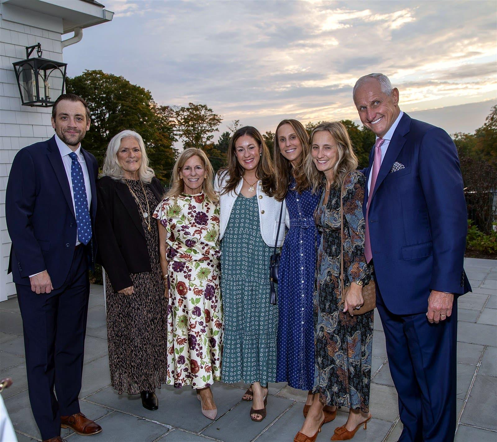 Seven guests posing together on the stone terrace under an evening sky.