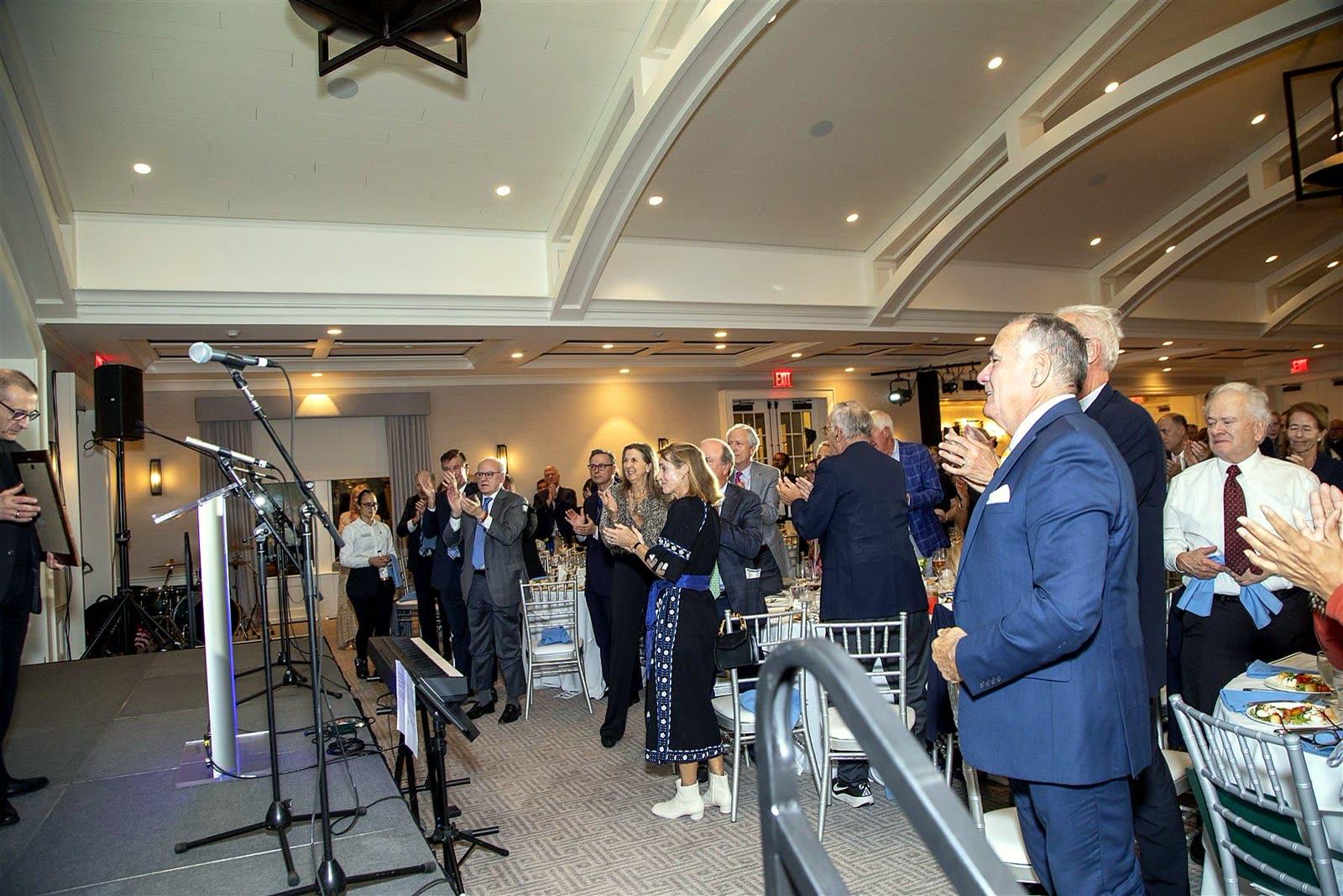 Guests rising from their tables to applaud toward the stage.