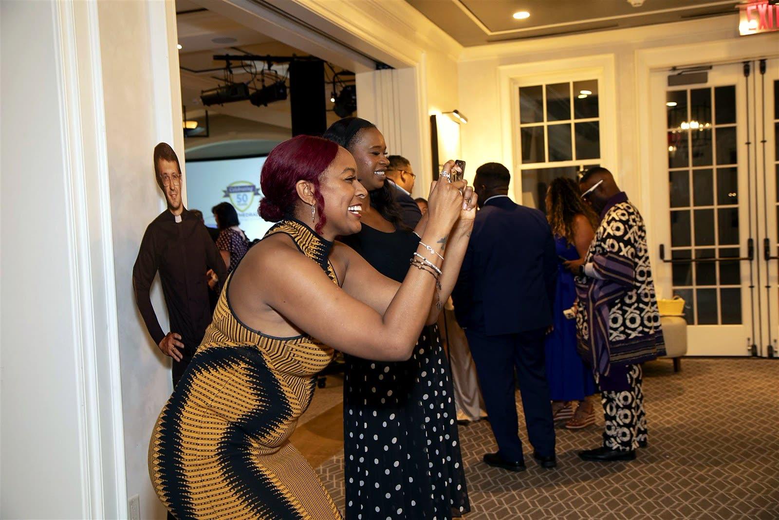 Guests laughing and taking phone photos with a life-size cardboard cutout in the hallway.