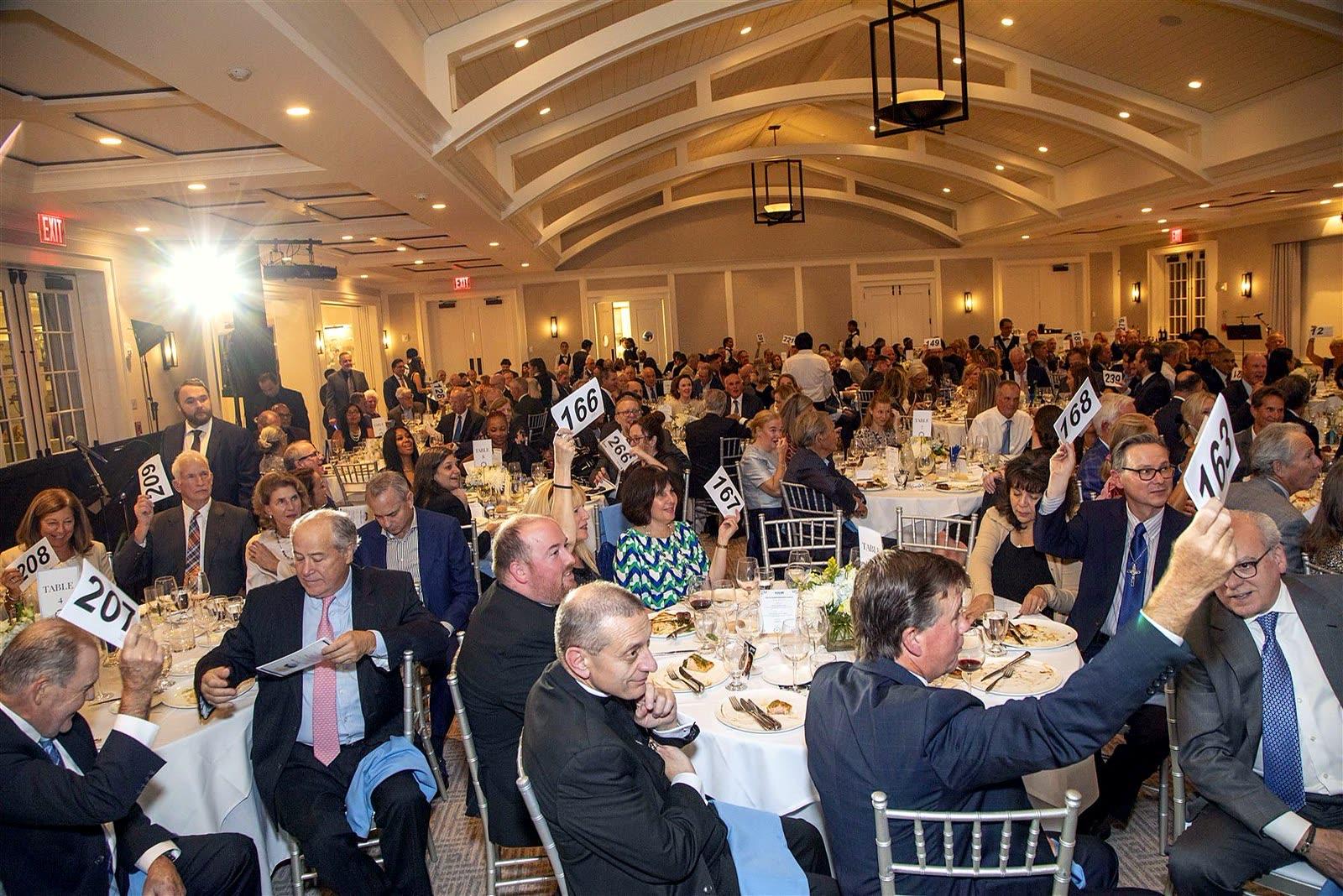 Guests across the ballroom raising numbered paddles during the paddle raise.