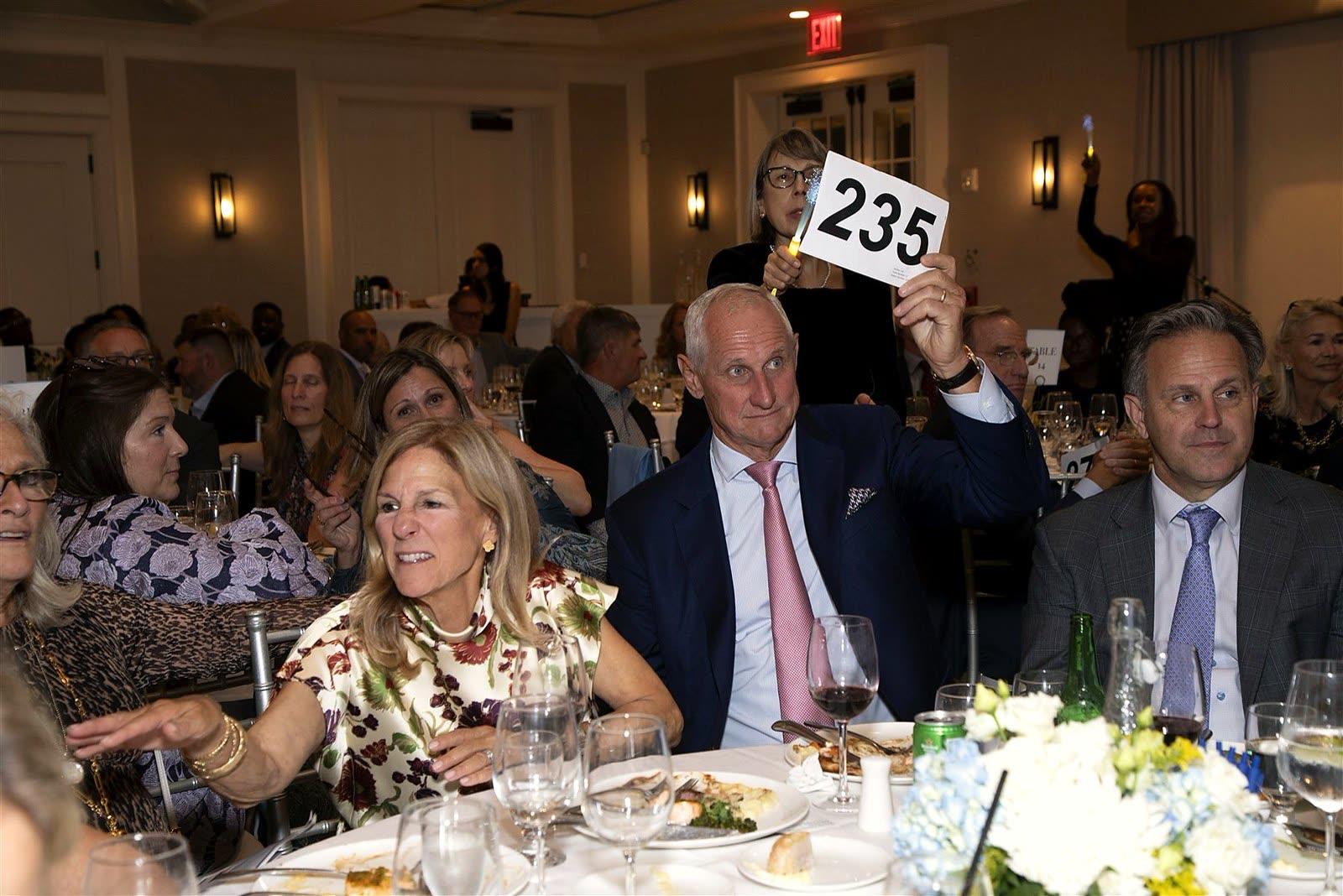 A guest raising a numbered paddle at a dinner table during the paddle raise.