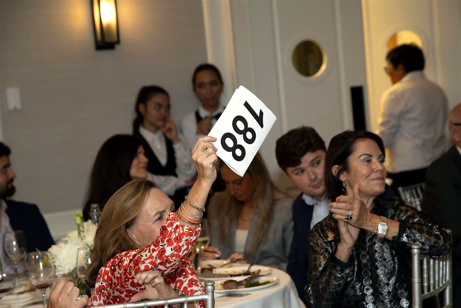 A guest raising a numbered paddle while a tablemate applauds.
